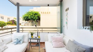 A balcony with a white sofa, a small table with a plant, and a view of buildings. - Vacation Home "La Tejita Beach House" with Mountain View, Shared Pool & Wi-Fi (La Tejita)