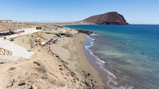 A beach with a rocky shoreline, a clear blue sea, and a prominent hill in the background. - Vacation Home "La Tejita Beach House" with Mountain View, Shared Pool & Wi-Fi (La Tejita)