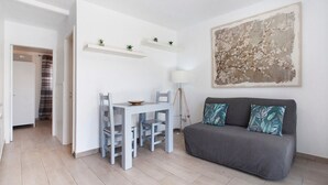 Una sala de estar moderna con un sofá gris, una mesa de comedor blanca y sillas, una lámpara y un cuadro abstracto grande en la pared.