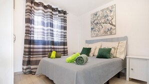 Un dormitorio con cama, almohadas, una mesita de noche, un cuadro y una cortina a rayas.