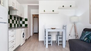 Una cocina compacta con lavadora, una mesa de comedor con sillas, una lámpara y un sofá.