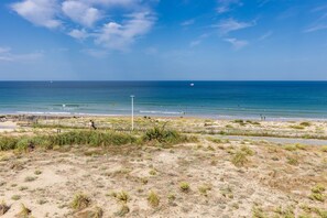 A beach with a sandy foreground, a wooden fence, and a clear blue sky.