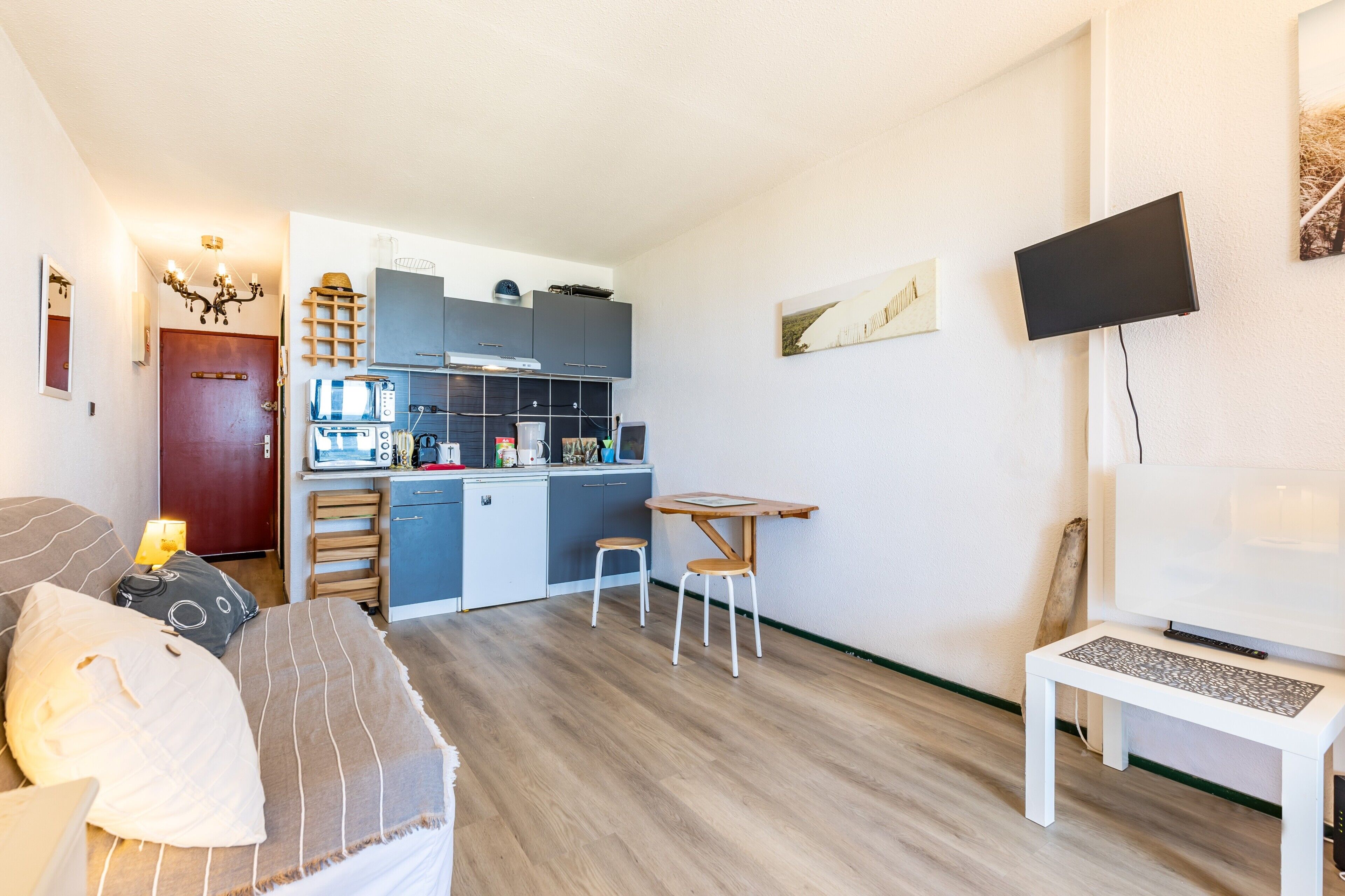 A compact living space with a kitchenette, a dining area, and a TV mounted on the wall.