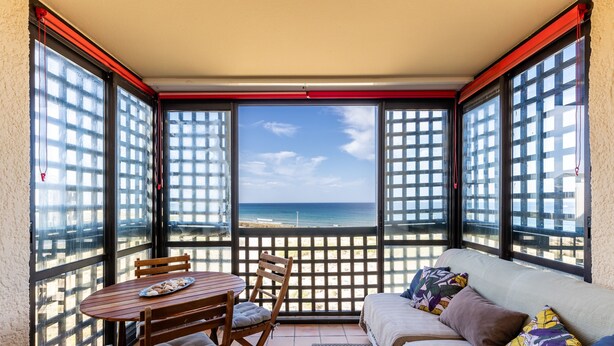 En balkon med et bord, stole, en sofa og udsigt til stranden.