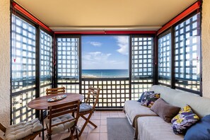 Een balkon met een tafel en stoelen, een bank en uitzicht op het strand.