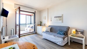 Et moderne værelse med sofa, lille bord, TV og en skydedør, der fører til et udendørs område.