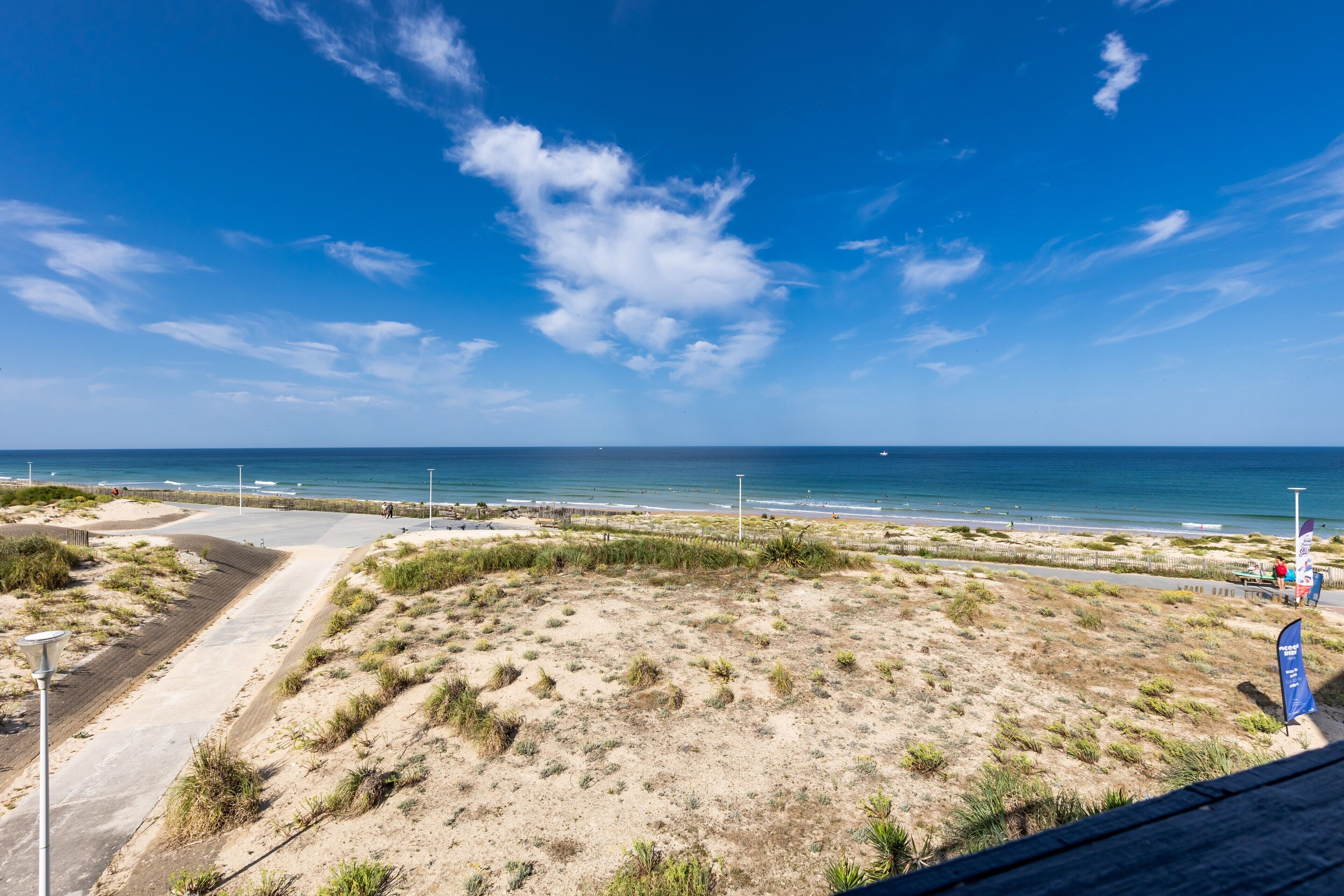 Een kustlandschap met heldere lucht, zandvlakte en een pad naar het strand.