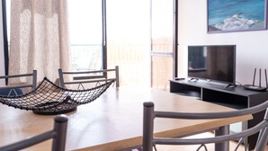 Ein Zimmer mit einem Holztisch, einem schwarzen gewebten Korb, einem Fernseher und einem Wandbild von Berg und Meer.
