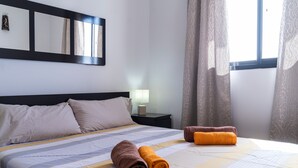 Ein Hotelzimmer mit Bett, Kissen, Nachttisch, Lampe und einem Fenster mit Vorhängen.