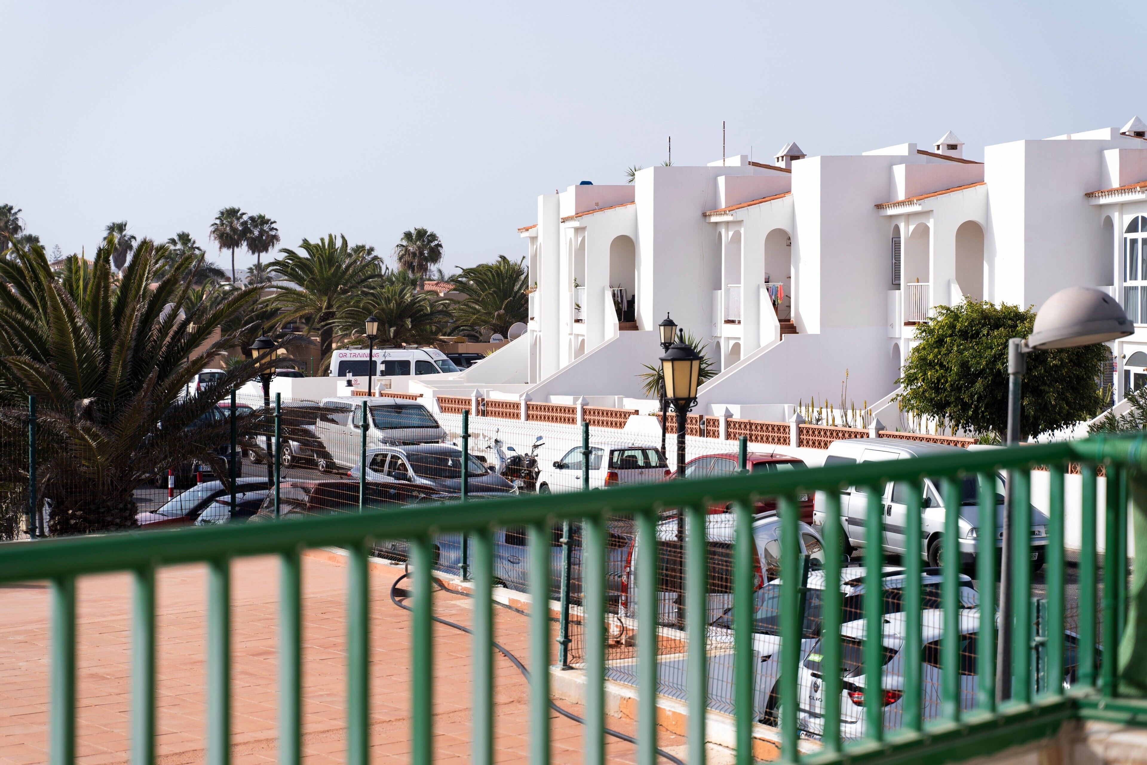 Un espace de stationnement avec des véhicules, un bâtiment blanc orné d’arches et des palmiers.