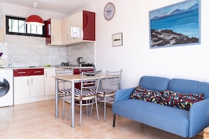 A compact kitchen with a dining area, a blue sofa, and a painting on the wall.