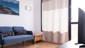 Ein Wohnzimmer mit einer Couch, einem kleinen Tisch, einem Fernseher und einem Fenster mit Vorhängen.