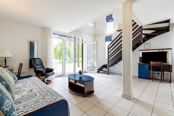 A spacious living area with a sofa, a coffee table, a chair, a desk, and a staircase.