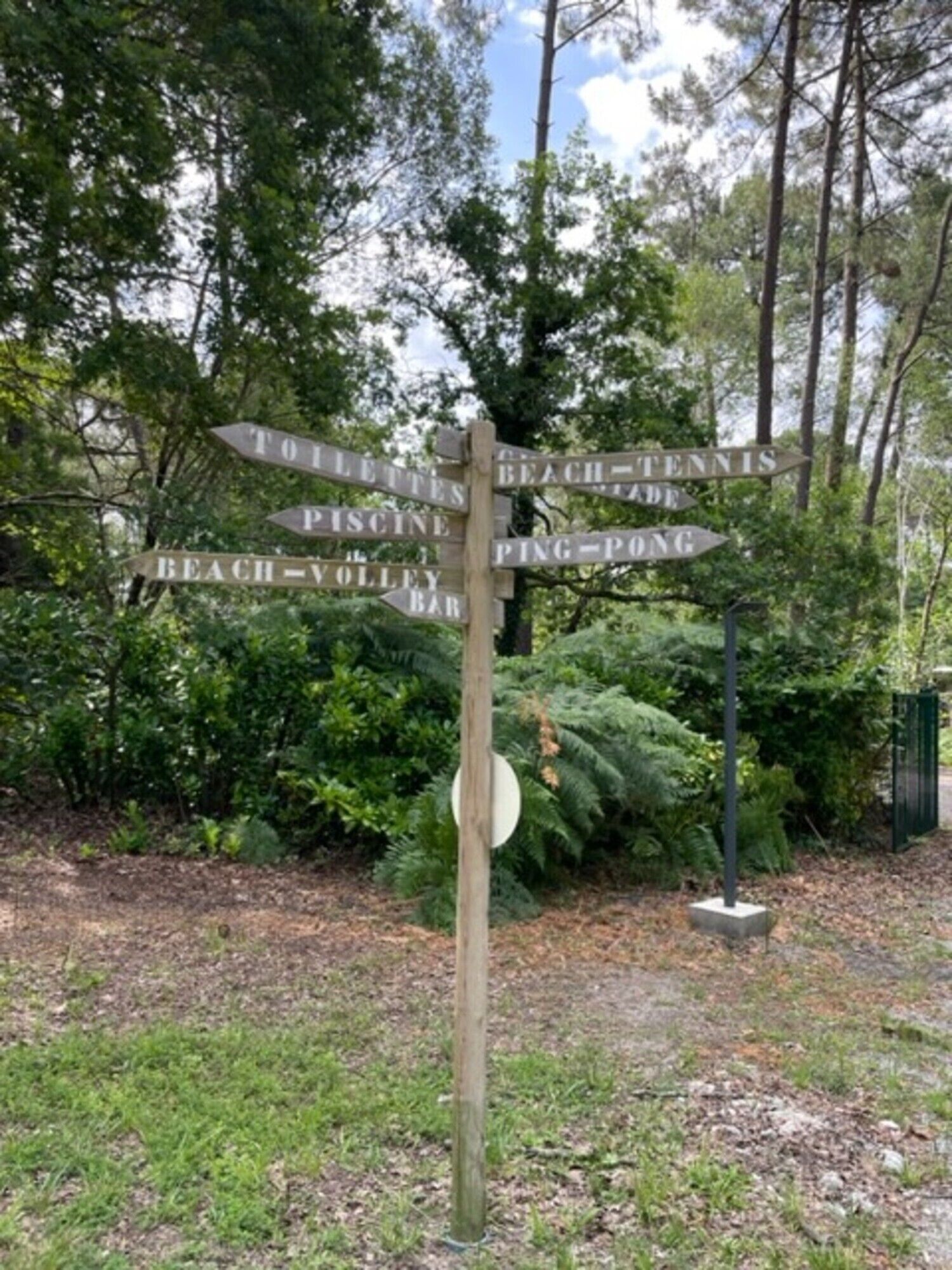 A wooden signpost with directional arrows pointing to various locations such as 'Beach,' 'Tennis,' 'Pine Pond,' and 'Bar.'