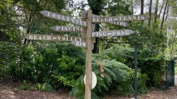 A wooden signpost with directional arrows pointing to various locations such as 'Beach,' 'Tennis,' 'Pine Pond,' and 'Bar.'