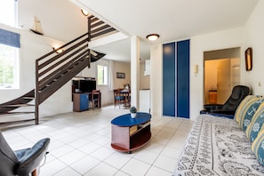 A modern living room with a staircase, a dining area, and a bedroom with a large bed.