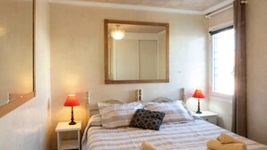 A hotel room with a bed, two bedside lamps, a mirror, and a window with curtains. - Holiday Home 'Los Barqueros 13' with Shared Pool, Private Terrace & Wi-Fi (Corralejo)