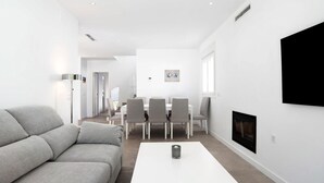 Ein modernes Wohnzimmer mit einer Couch, einem weißen Couchtisch, einem Essbereich mit Stühlen und einem Kamin.