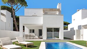 Eine moderne Villa mit Schwimmbad, Sitzgelegenheiten im Freien und einem großen Baum.