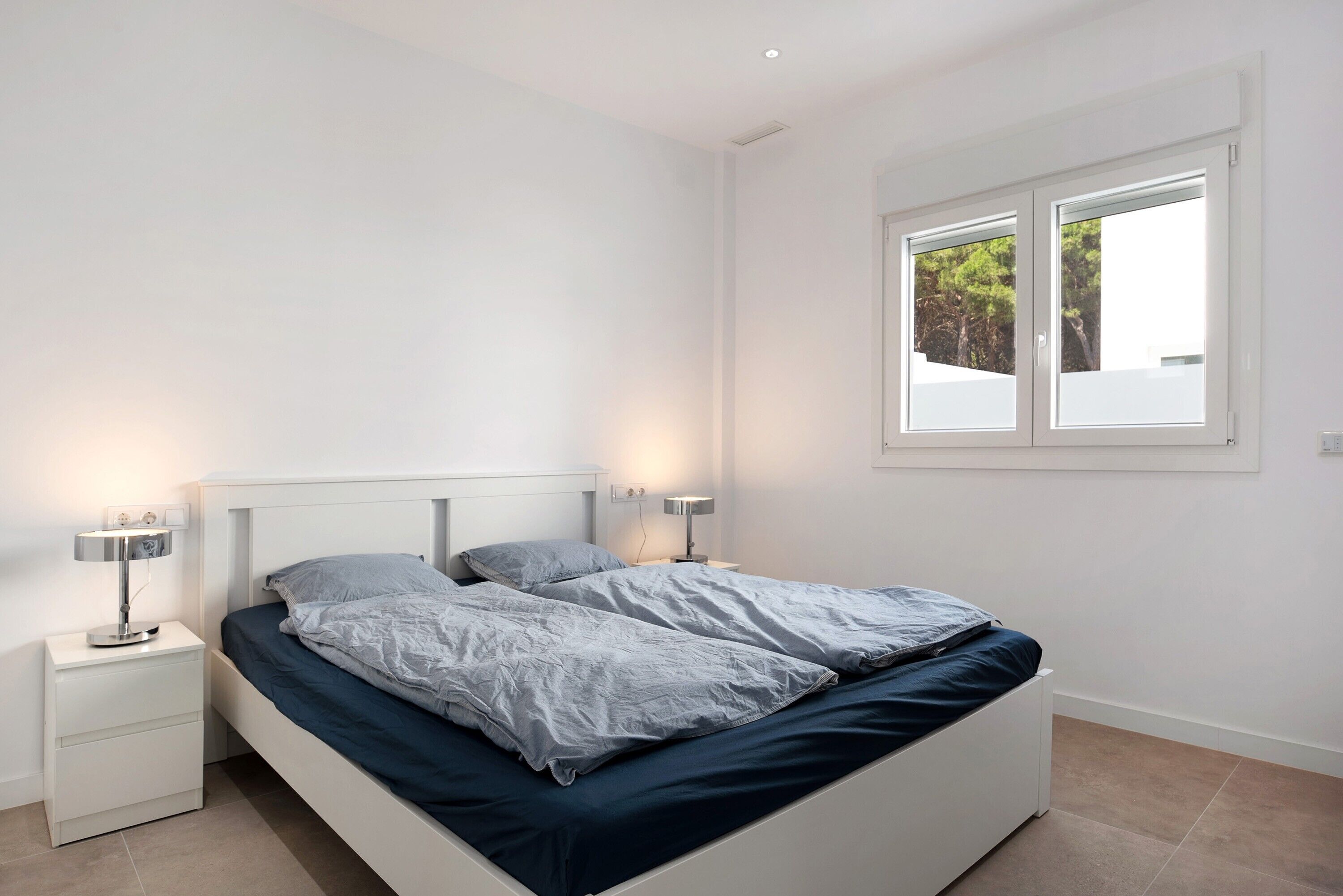 Une chambre à coucher comprenant un lit, deux tables de chevet, une fenêtre et une petite table.