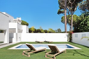 Un espace piscine extérieur moderne, doté de chaises longues, d’une piscine et d’un bâtiment blanc aux grandes fenêtres.