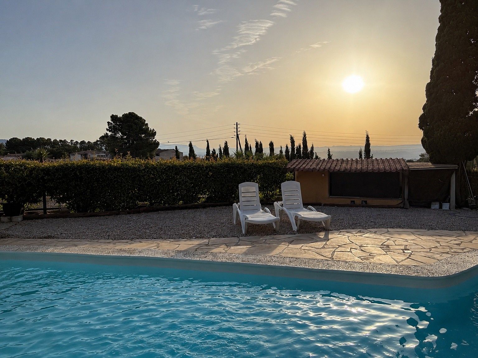 A swimming pool with lounge chairs and a view of the sunset.