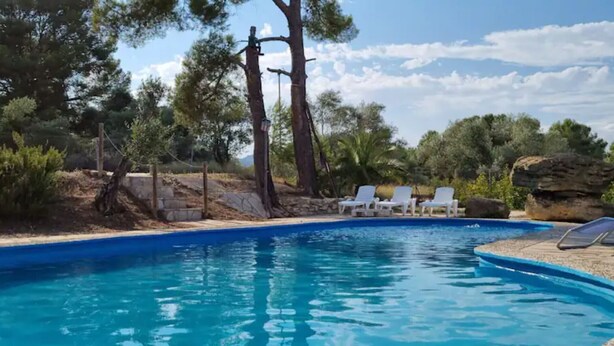 A swimming pool with lounge chairs, surrounded by trees and a rocky landscape.