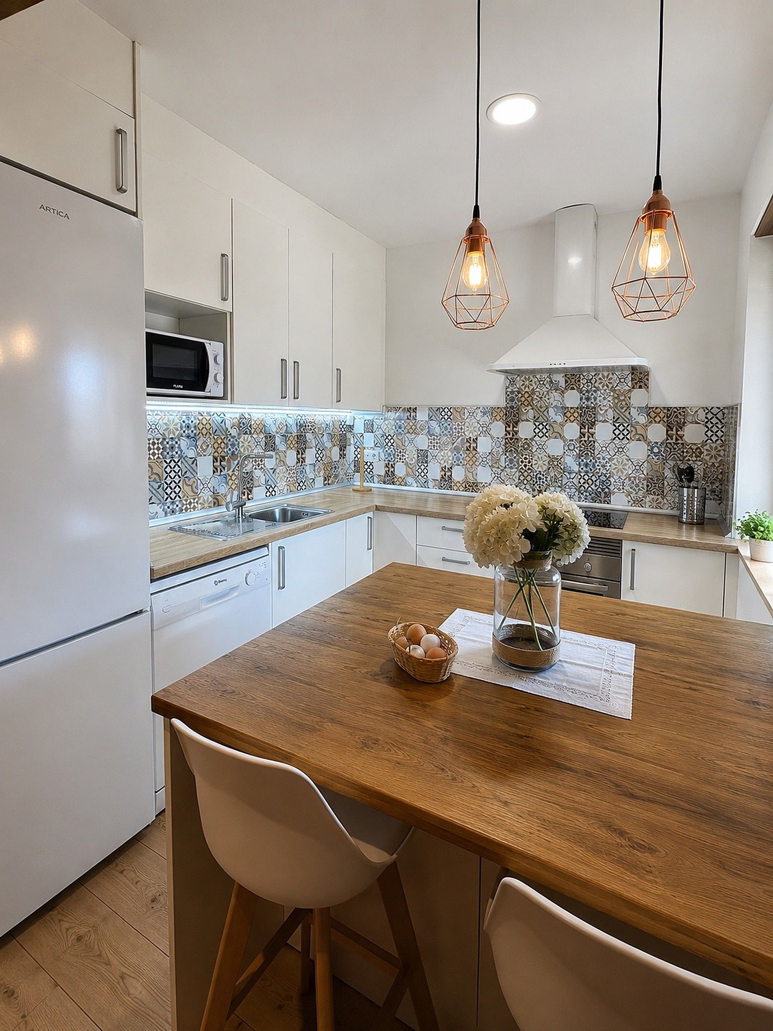 A modern kitchen with white cabinetry, a wooden island, and a patterned backsplash.