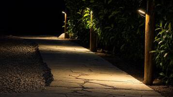 Een verlicht pad 's nachts, met stenen bestrating, omringd door groen en verlicht door lantaarns.