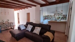 A living room with a sofa, a dining table with chairs, and a kitchen in the background.