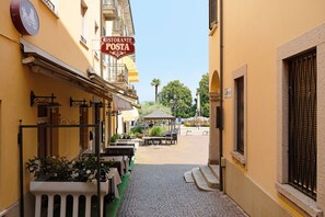 Una calle estrecha con mesas al aire libre, un letrero de restaurante y un pabellón a lo lejos.