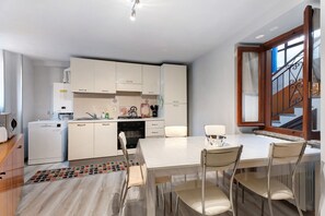A modern kitchen with white cabinets, a dining table with chairs, and a staircase with a wooden railing.