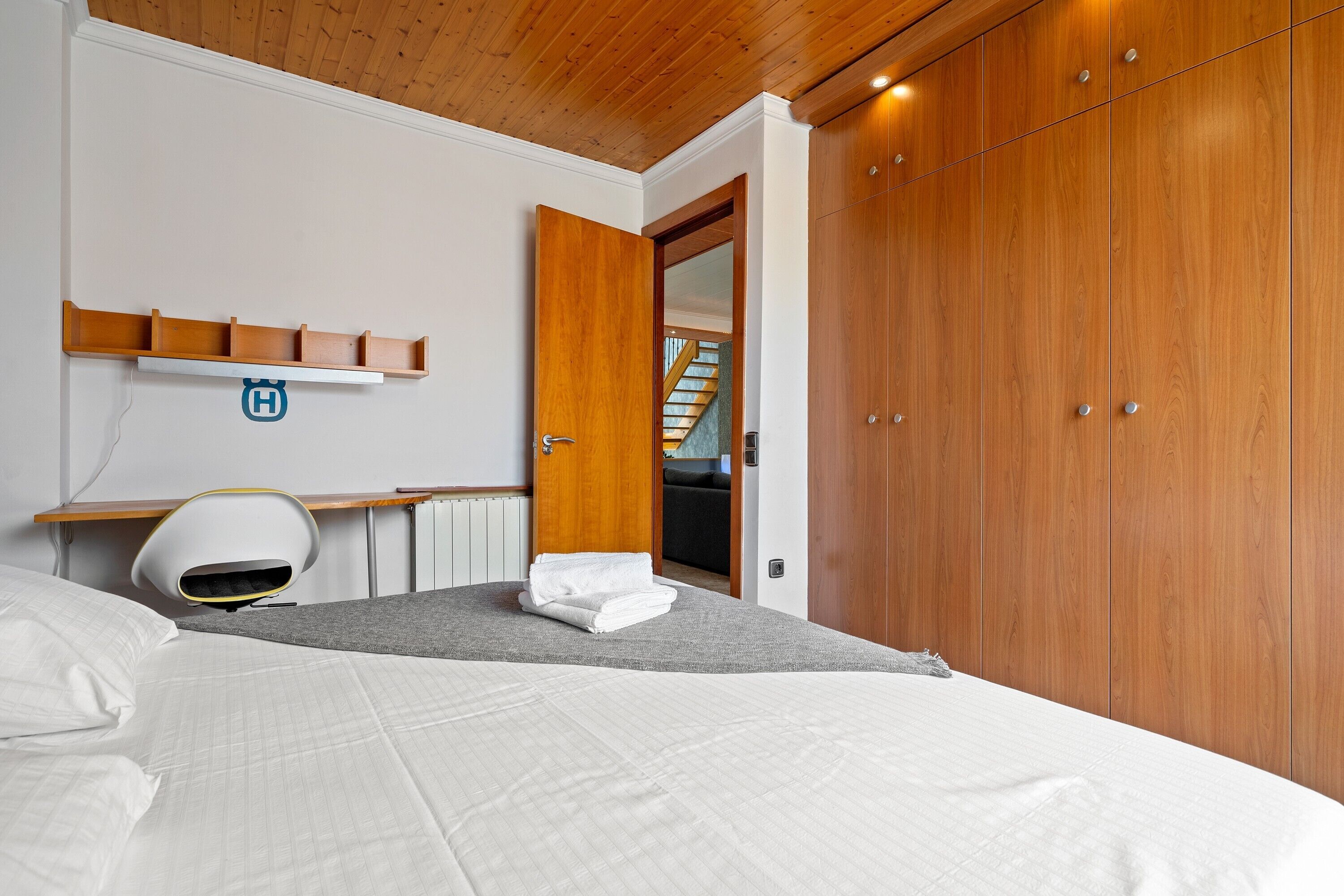 Een slaapkamer met een bed, een bureau, een stoel, een kledingkast en een deur naar een andere kamer.