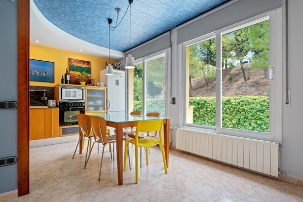 A modern kitchen with a dining area, large windows, and a view of greenery.