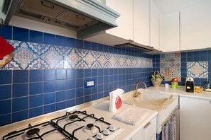 A kitchen with blue patterned tiles, a gas stove, a sink, and a countertop with various items.