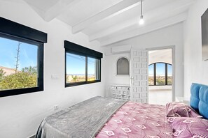 A bedroom with a bed, a dresser, a bench, and a view of the outdoors.