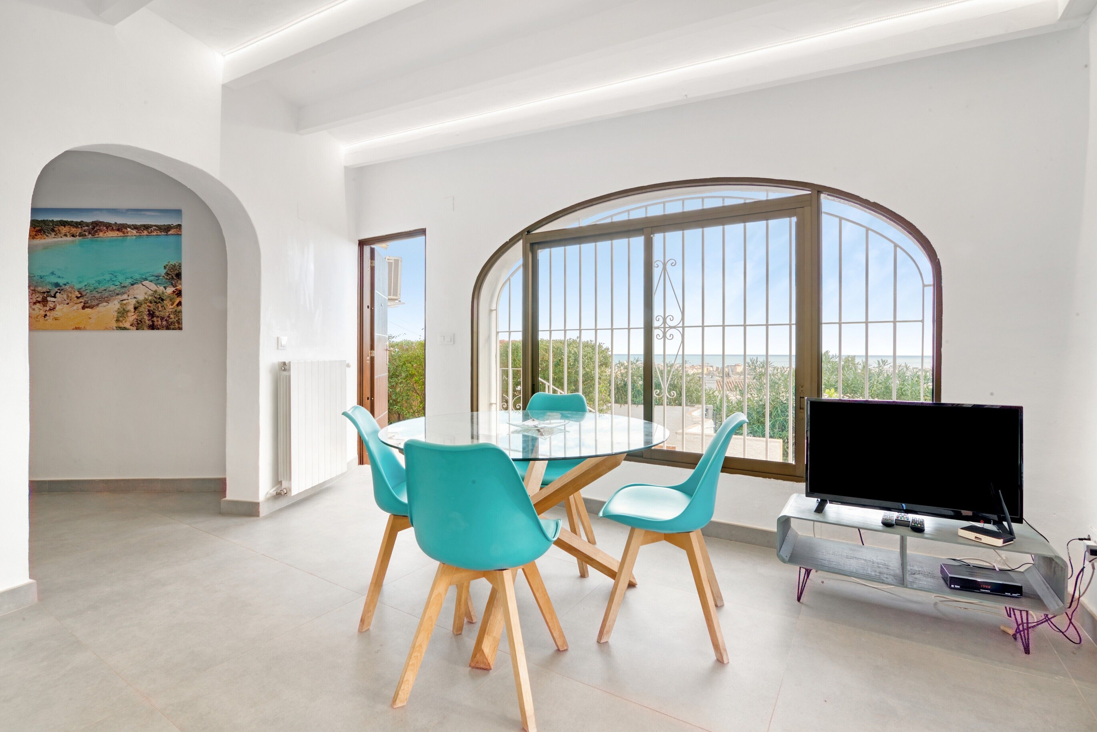 Ein moderner Essbereich mit einem runden Tisch und Stühlen, einem Fernseher auf einem Schrank und einem großen Bogenfenster mit Aussicht.