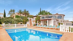 A swimming pool with lounge chairs, a white fence, and a building with large windows and a balcony. - Villa 'Ericito' with Private Pool, Wi-Fi and Air Conditioning (Dénia)