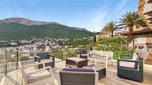 A terrace with wicker furniture, a glass balustrade, and a view of a town and mountains. - Villa 'Ericito' with Private Pool, Wi-Fi and Air Conditioning (Dénia)