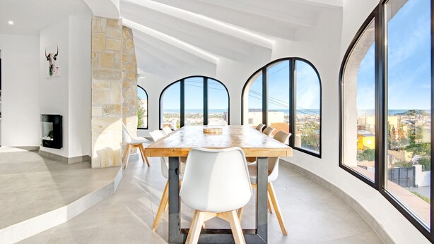 A modern dining room with a large table, white chairs, and large windows offering a city view. - Villa 'Ericito' with Private Pool, Wi-Fi and Air Conditioning (Dénia)