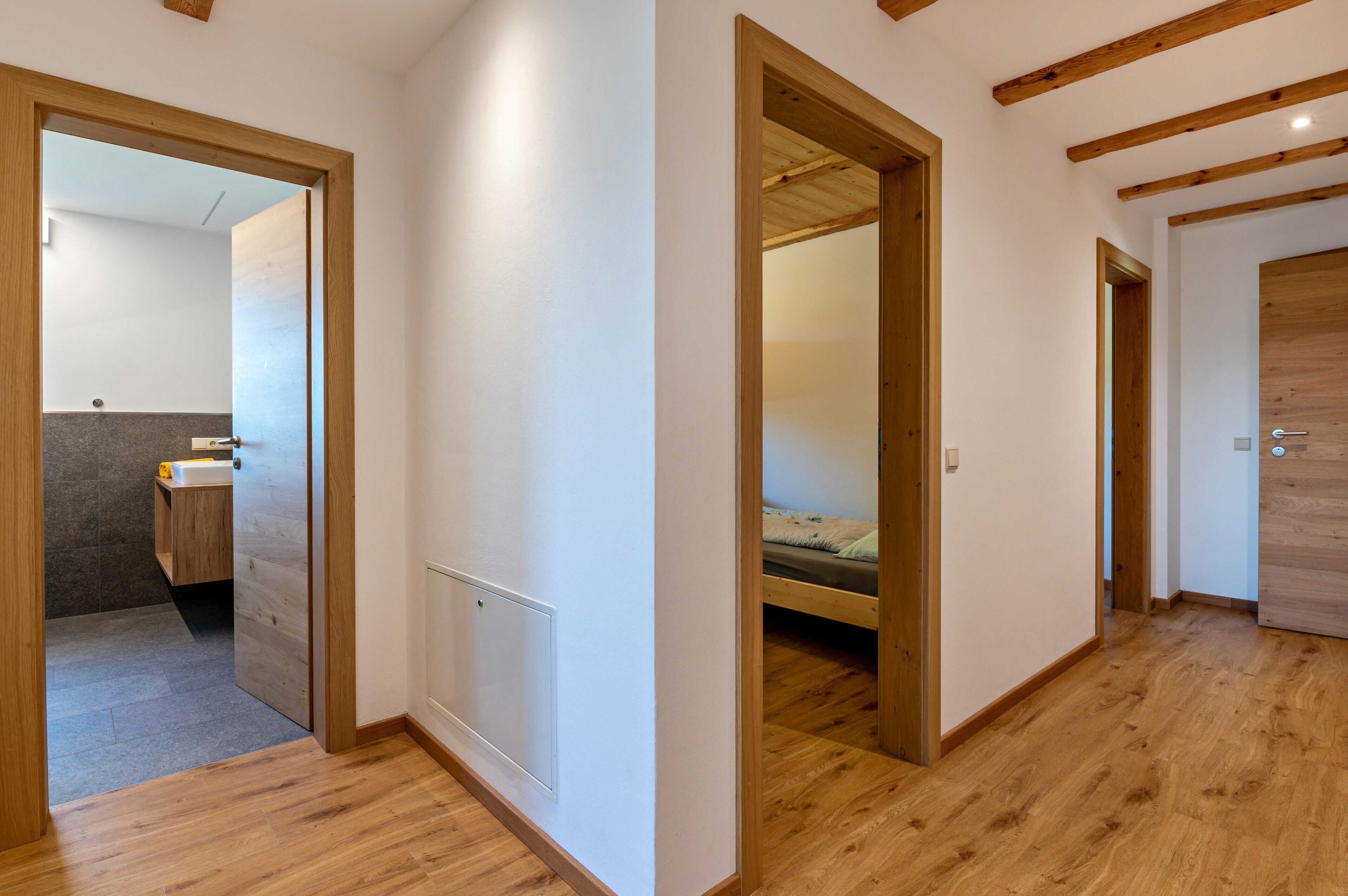 A hallway with wooden floors and doors leading to a bathroom and a bedroom.