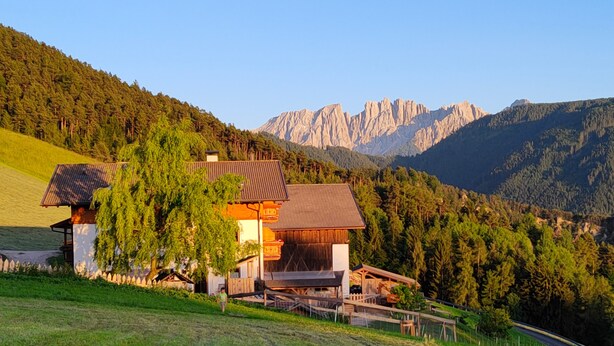 Una casa con tetto spiovente, rivestimento in legno e vista sulle montagne.