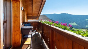 Un balcone in legno con tavolo e sedie, affacciato su un paesaggio montano.