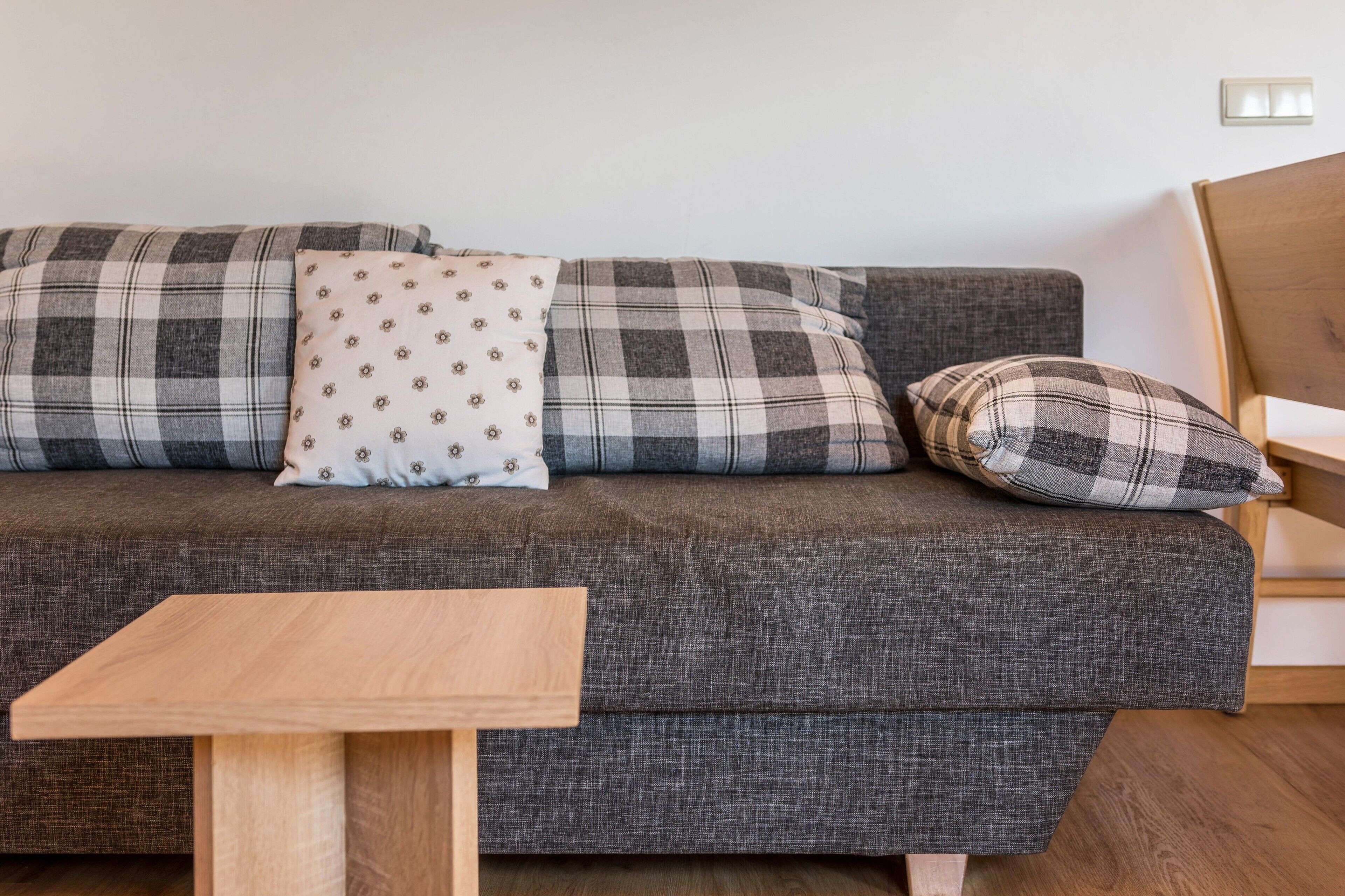 Ein graues Sofa mit karierten Kissen, ein kleiner Holztisch und ein Holzstuhl.