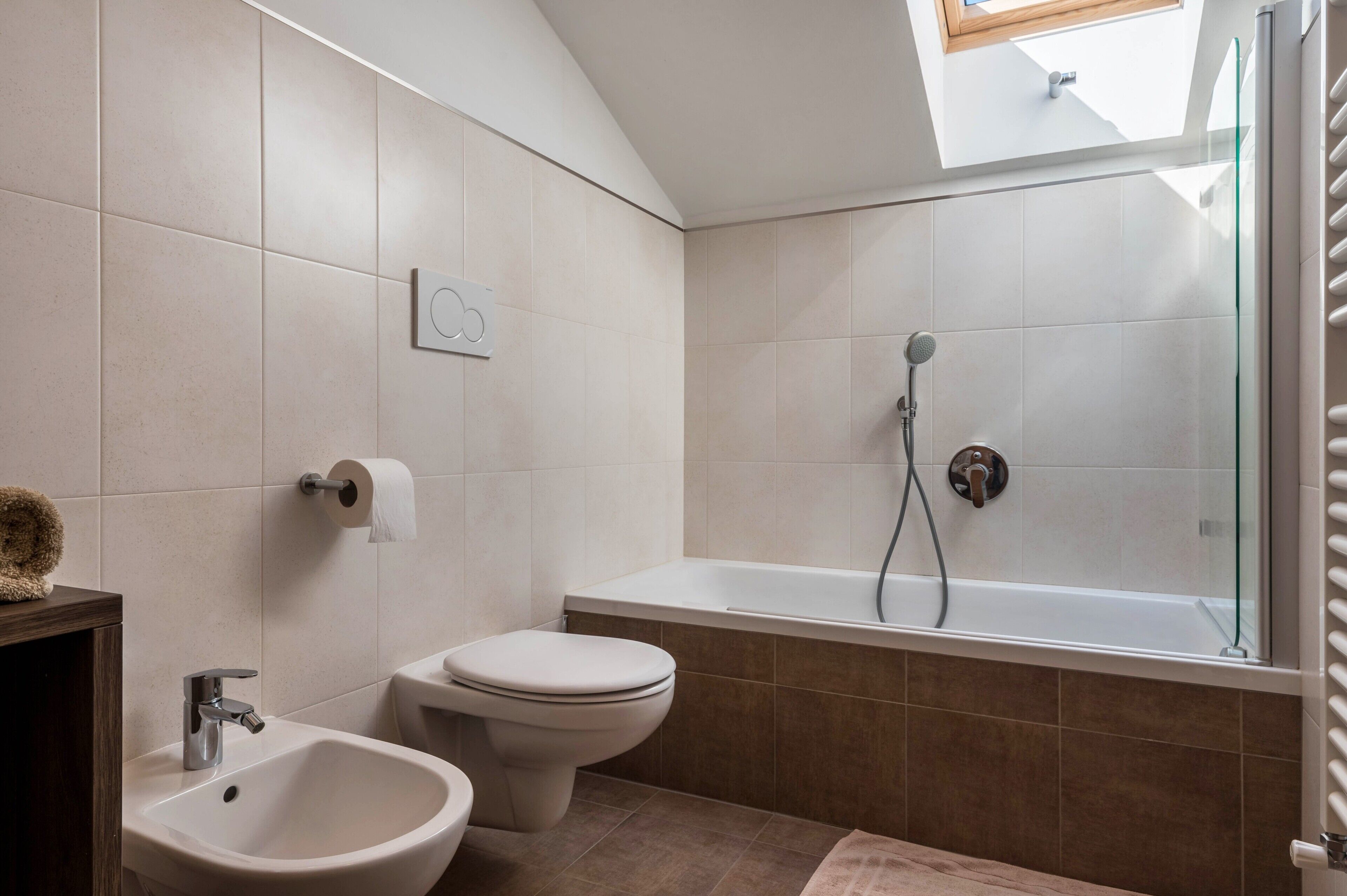 Une salle de bain moderne équipée d’une baignoire, de toilettes, d’un bidet et d’une lucarne.