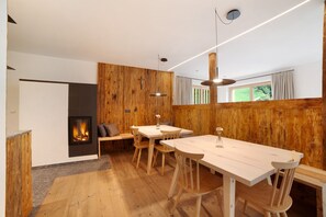 Un intérieur moderne avec un mur en bois, une cheminée, un coin repas avec des chaises en bois et une grande fenêtre.