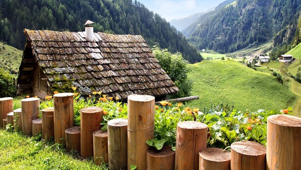 A rustic wooden house with a sloped roof, surrounded by a wooden fence and vibrant flowers. - Apartment 'Herrischner 1' with Mountain View, Private Terrace and Wi-Fi (Moos in Passeier)