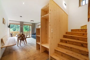 A wooden staircase, a dining area with a bench and chairs, and a view of the outdoors through large windows.