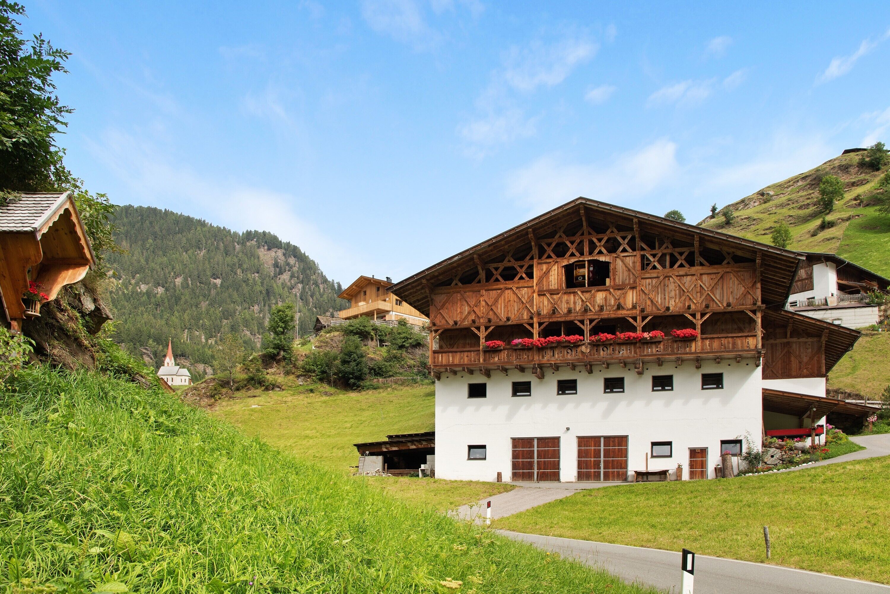 Ein traditionelles Holzchalet mit Balkon, umgeben von üppiger Vegetation und einer Bergkulisse.