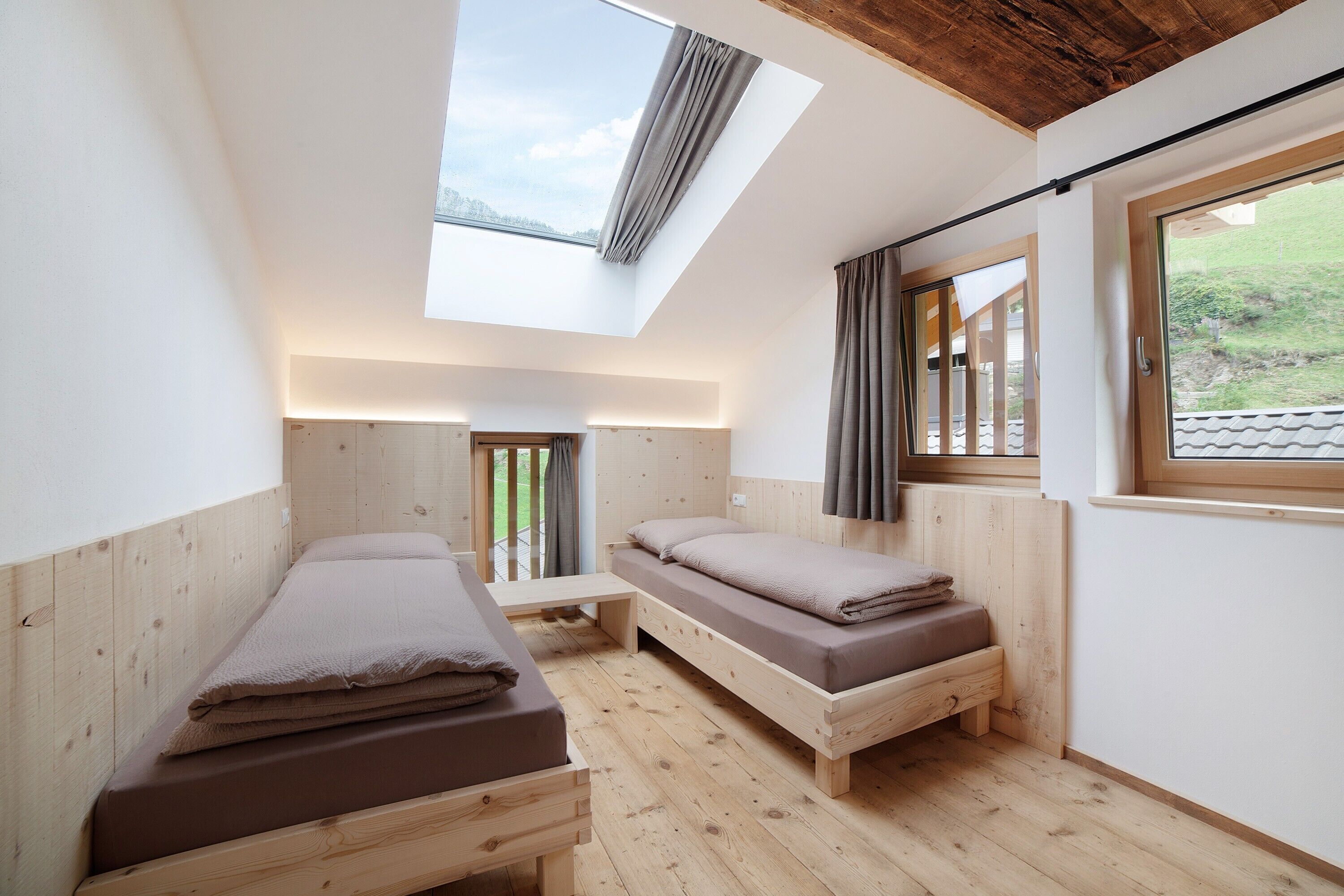 Une petite pièce avec deux lits en bois, un puits de lumière et une fenêtre avec des rideaux.